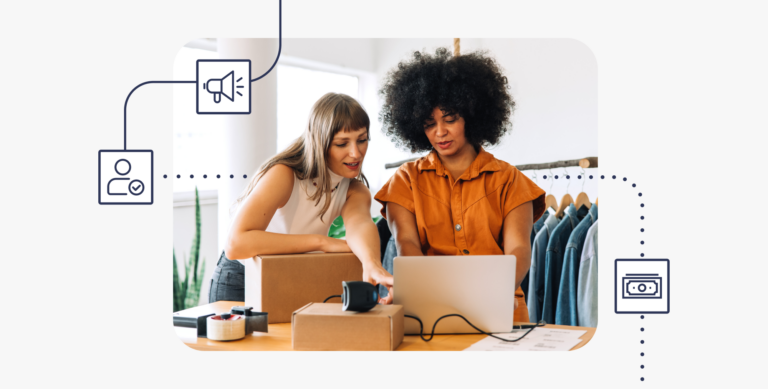 Two women sit at a computer with shipping boxes to represent one friend referring another to ShipStation.